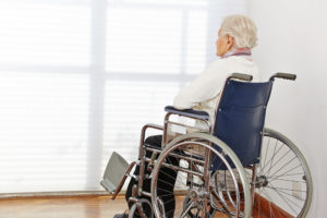 elderly person in a wheelchair facing a window with the blinds drawn