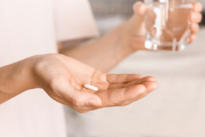 person holding a pill and glass of water